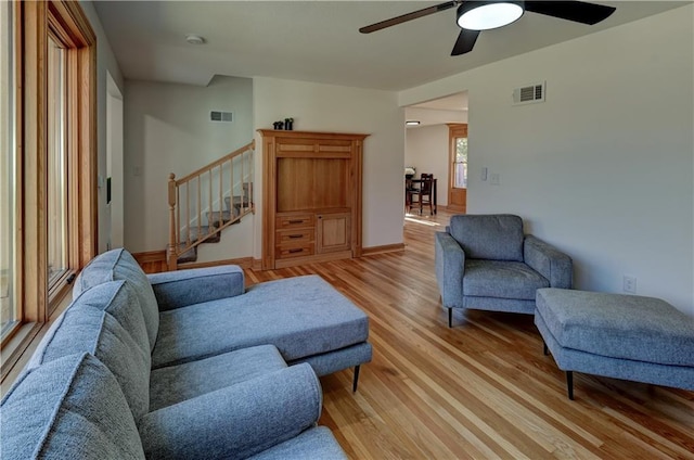 living room with light wood-type flooring, stairs, visible vents, and a ceiling fan