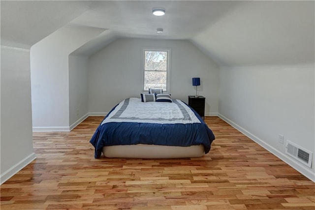 bedroom with visible vents, vaulted ceiling, light wood-style flooring, and baseboards