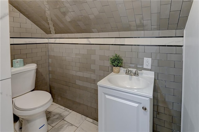 half bathroom featuring tile walls, marble finish floor, vanity, and toilet