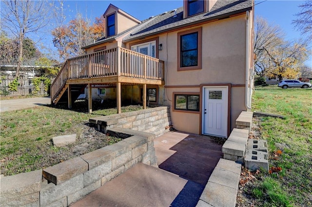 rear view of property featuring a yard, a wooden deck, stairway, and stucco siding