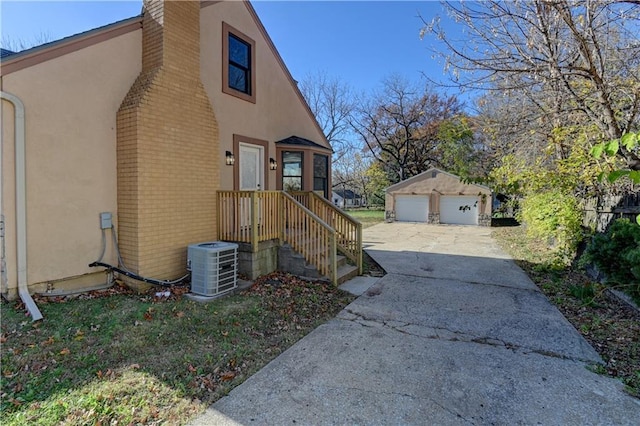 view of side of property with an outbuilding, brick siding, a detached garage, stucco siding, and central air condition unit