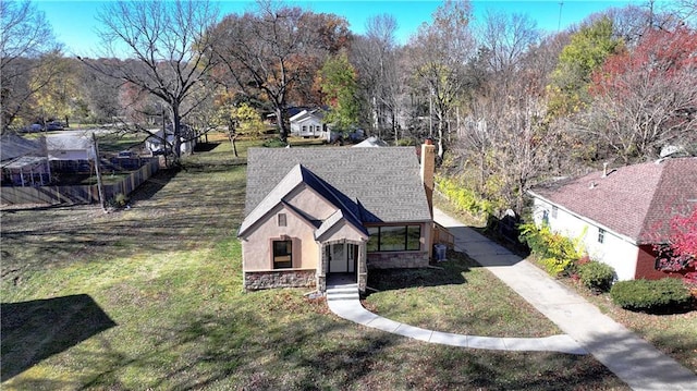 view of front of home with a shingled roof, stone siding, a chimney, a front lawn, and stucco siding