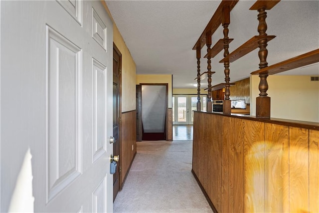 hall featuring a textured ceiling, wooden walls, and light carpet