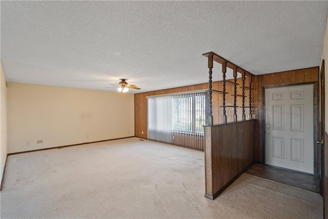 carpeted spare room with wood walls, ceiling fan, and a textured ceiling