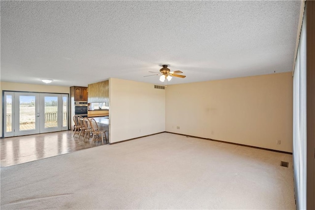 unfurnished living room featuring light carpet, french doors, a textured ceiling, and ceiling fan