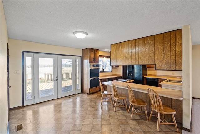 kitchen featuring french doors, sink, a kitchen breakfast bar, kitchen peninsula, and black appliances