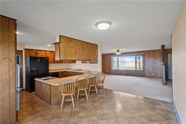 kitchen featuring a kitchen breakfast bar, wooden walls, ceiling fan, black fridge with ice dispenser, and kitchen peninsula