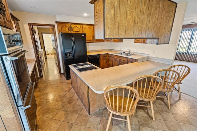 kitchen featuring a kitchen bar, kitchen peninsula, sink, and black appliances