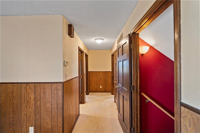 hallway featuring wood walls, light colored carpet, and a textured ceiling