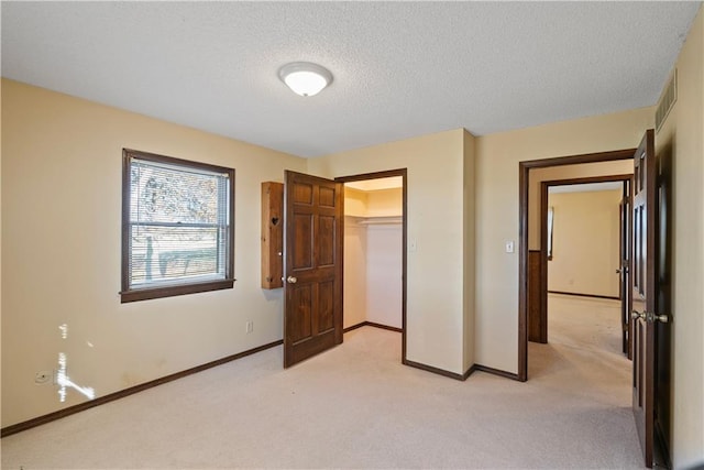 unfurnished bedroom featuring a textured ceiling, a walk in closet, light carpet, and a closet