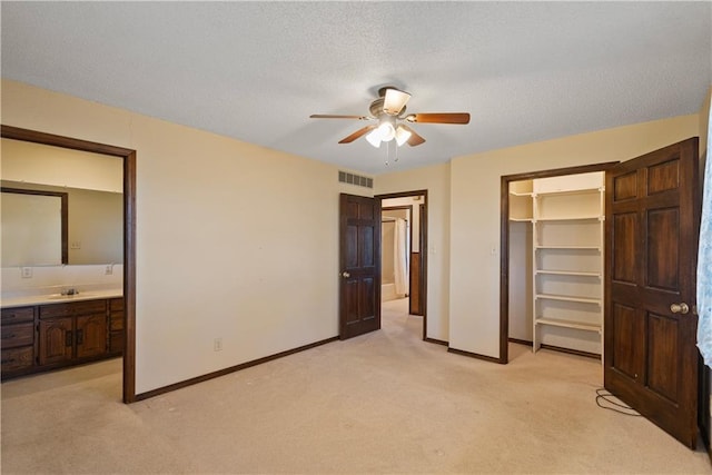 unfurnished bedroom featuring ceiling fan, light colored carpet, a walk in closet, and sink