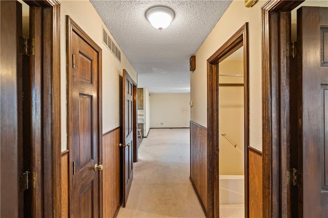 corridor featuring a textured ceiling, light colored carpet, and wood walls