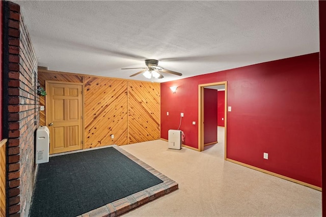 spare room featuring carpet flooring, wood walls, ceiling fan, and a textured ceiling