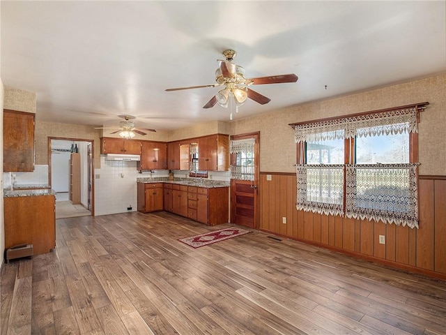 kitchen featuring wood walls, sink, ceiling fan, and light hardwood / wood-style floors