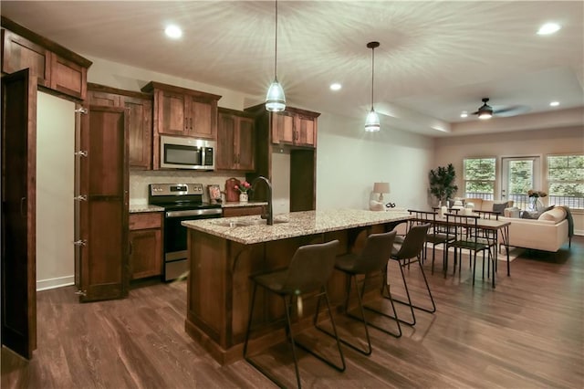 kitchen featuring light stone countertops, sink, dark hardwood / wood-style floors, decorative light fixtures, and appliances with stainless steel finishes