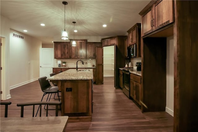 kitchen with electric range, light stone countertops, an island with sink, decorative light fixtures, and dark hardwood / wood-style flooring