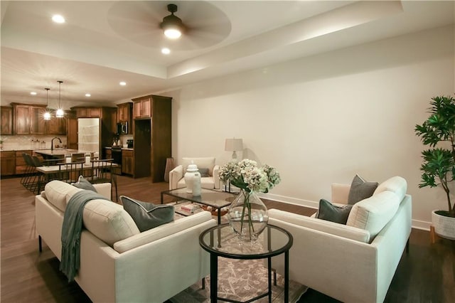 living room featuring a tray ceiling, ceiling fan, and dark wood-type flooring