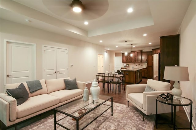 living room with a raised ceiling, ceiling fan, dark hardwood / wood-style flooring, and sink