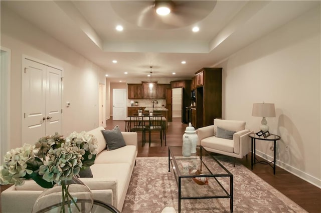 living room with a tray ceiling, ceiling fan, sink, and dark hardwood / wood-style floors