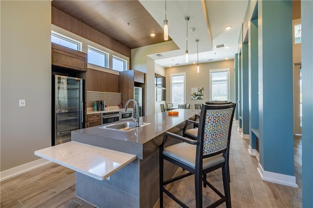 kitchen featuring plenty of natural light, sink, light hardwood / wood-style flooring, an island with sink, and decorative light fixtures