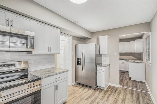 kitchen featuring tasteful backsplash, light hardwood / wood-style floors, light stone counters, white cabinetry, and stainless steel appliances