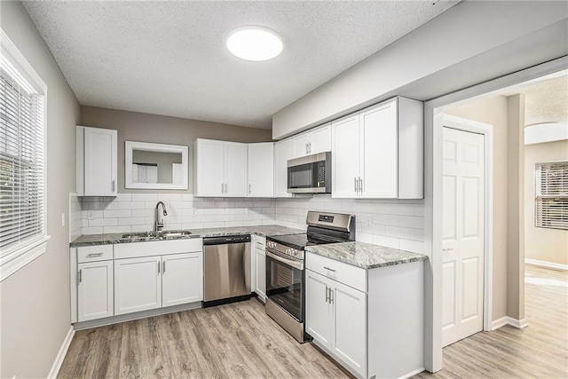 kitchen with white cabinets, light hardwood / wood-style floors, a textured ceiling, and appliances with stainless steel finishes