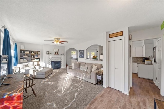 living room with hardwood / wood-style floors, a textured ceiling, ceiling fan, and a tiled fireplace