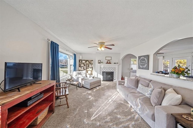 carpeted living room featuring a tile fireplace, ceiling fan, french doors, and a textured ceiling