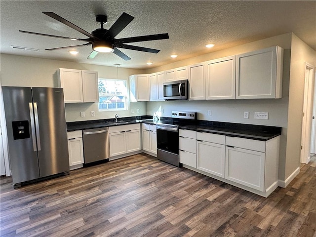 kitchen with dark wood-type flooring, white cabinets, sink, a textured ceiling, and appliances with stainless steel finishes