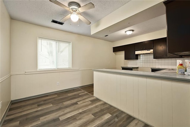 kitchen with decorative backsplash, dark brown cabinetry, a textured ceiling, dark hardwood / wood-style flooring, and kitchen peninsula