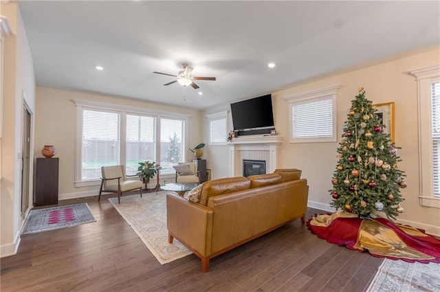 living room with a tile fireplace, ceiling fan, and dark wood-type flooring