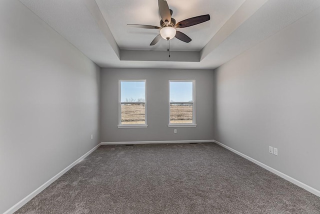 carpeted spare room with a raised ceiling and ceiling fan