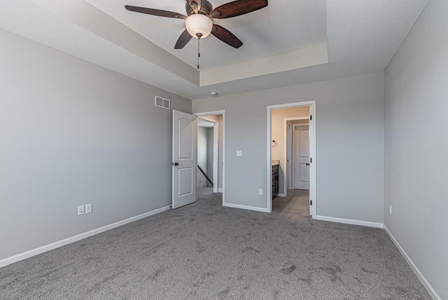 unfurnished bedroom featuring a raised ceiling, ceiling fan, light colored carpet, and ensuite bathroom