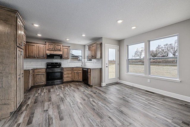 kitchen with a wealth of natural light, dark hardwood / wood-style flooring, and black appliances