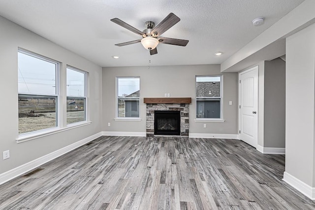 unfurnished living room with ceiling fan, a healthy amount of sunlight, wood-type flooring, and a fireplace