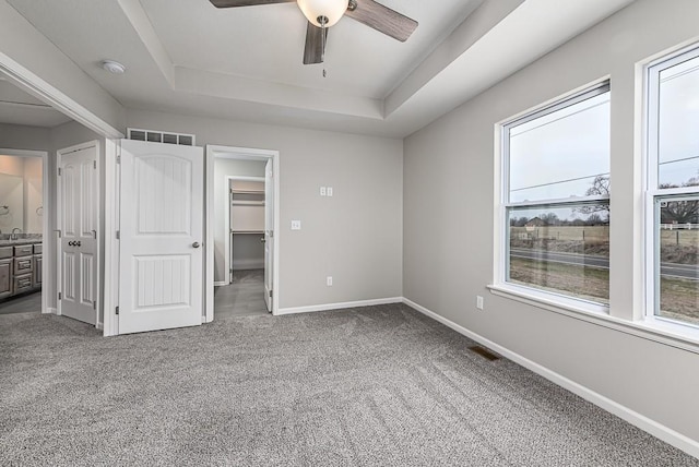 unfurnished bedroom featuring a spacious closet, ceiling fan, a raised ceiling, and carpet floors