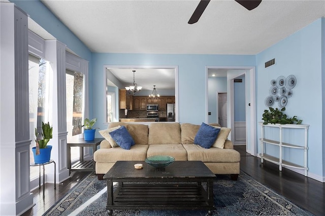 living room with ceiling fan with notable chandelier and dark hardwood / wood-style floors