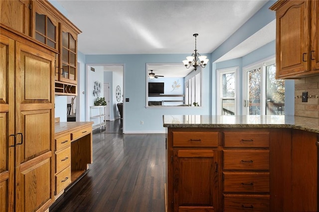 kitchen featuring light stone countertops, dark wood-type flooring, pendant lighting, decorative backsplash, and ceiling fan with notable chandelier