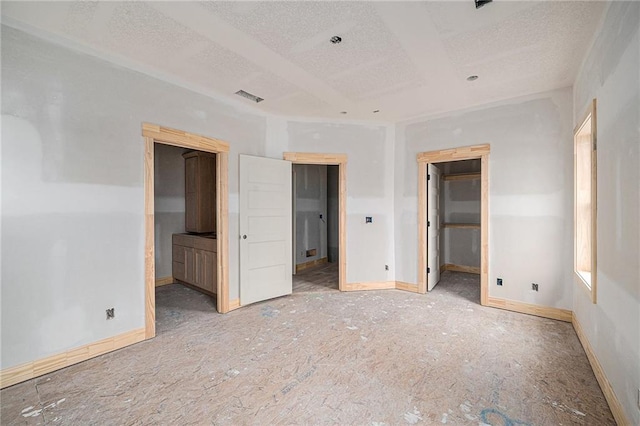 unfurnished bedroom with a walk in closet, ensuite bathroom, and a textured ceiling