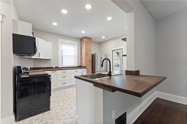 kitchen with a healthy amount of sunlight, white cabinetry, range with electric cooktop, and stainless steel refrigerator