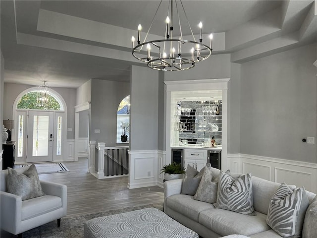 living room featuring a tray ceiling, beverage cooler, wood-type flooring, and an inviting chandelier