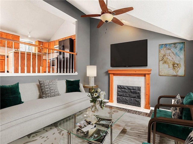 living room with vaulted ceiling, ceiling fan, and a tiled fireplace