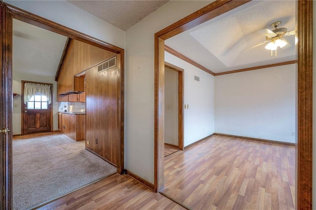 hallway with crown molding, wooden walls, light hardwood / wood-style floors, and a textured ceiling