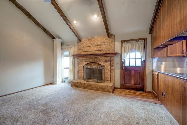 unfurnished living room with vaulted ceiling with beams, wooden walls, a fireplace, and light colored carpet