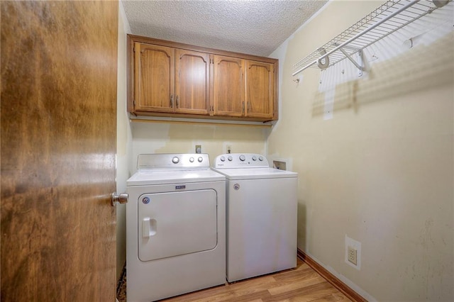 washroom with cabinets, light wood-type flooring, a textured ceiling, and washing machine and clothes dryer