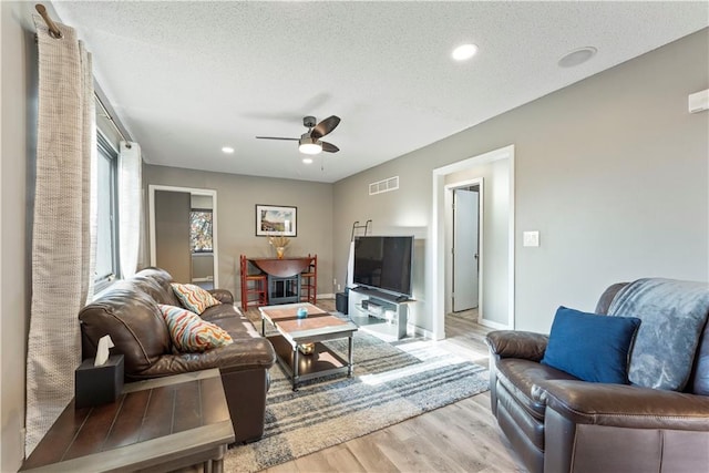 living room featuring a fireplace, a textured ceiling, light hardwood / wood-style flooring, and ceiling fan