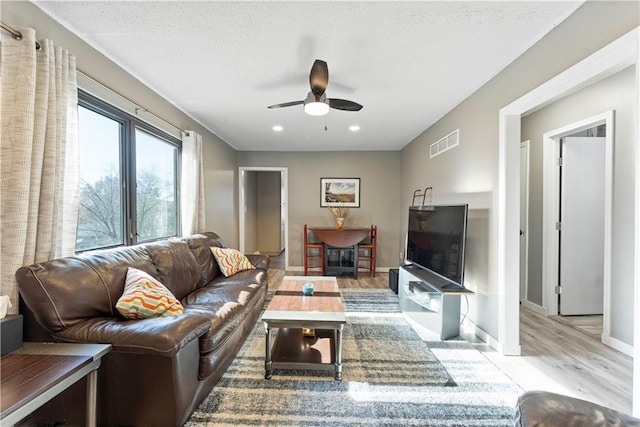 living room featuring ceiling fan, a textured ceiling, and light wood-type flooring