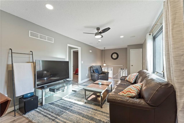 living room with ceiling fan, light wood-type flooring, a textured ceiling, and a wealth of natural light