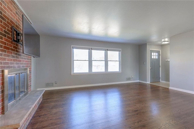 unfurnished living room featuring dark hardwood / wood-style floors and a brick fireplace