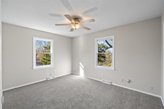 unfurnished room featuring ceiling fan, dark carpet, and a wealth of natural light